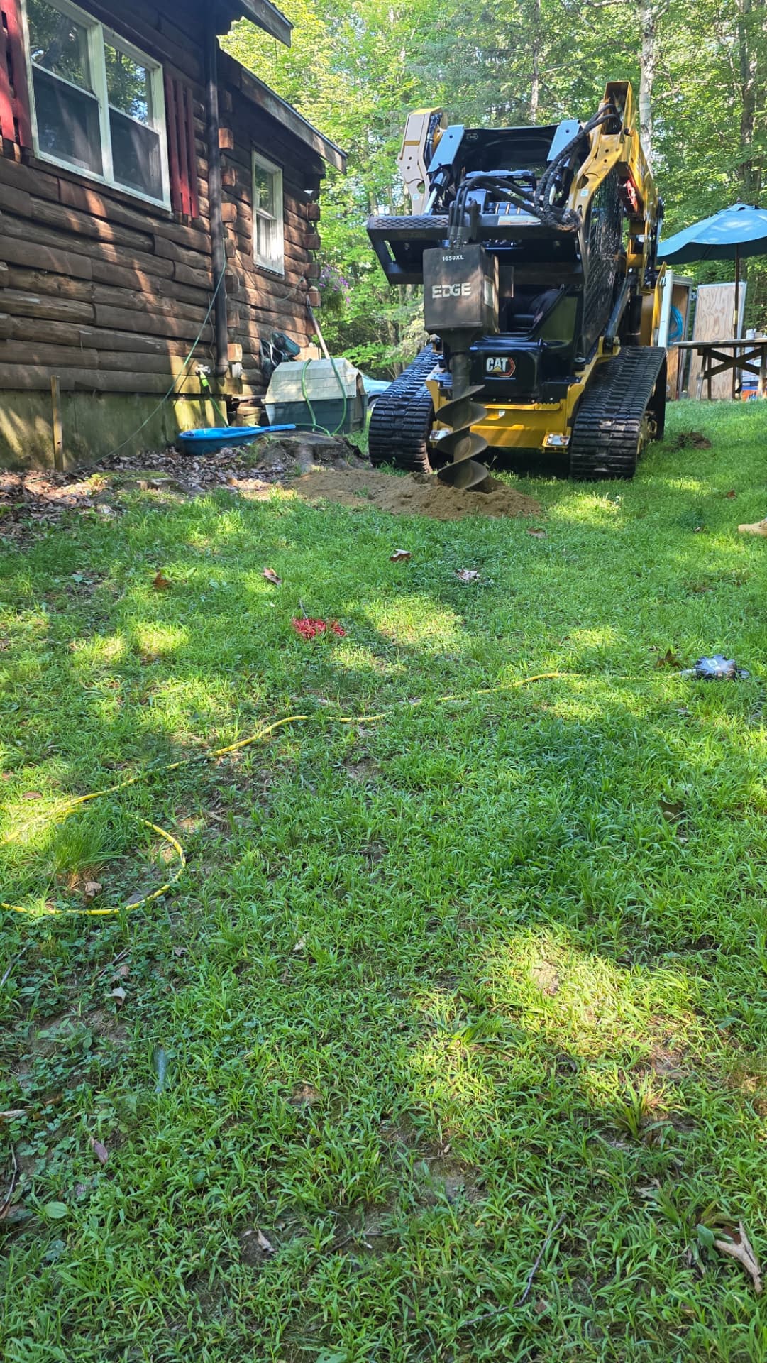 Post hole auger digging beside a log home in the woods